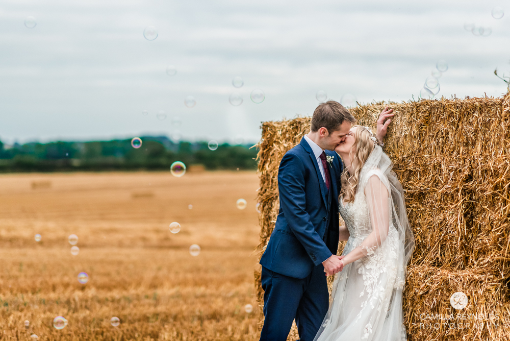 bride and groom kissing by hay bale with bubbles cotswold  wedding photo