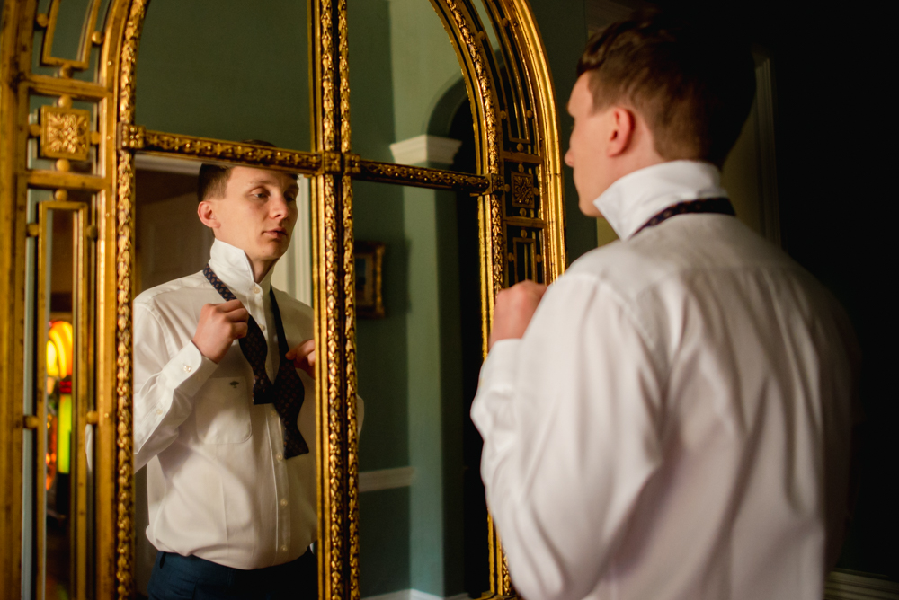 groom looking into mirror doing tie wedding photography 