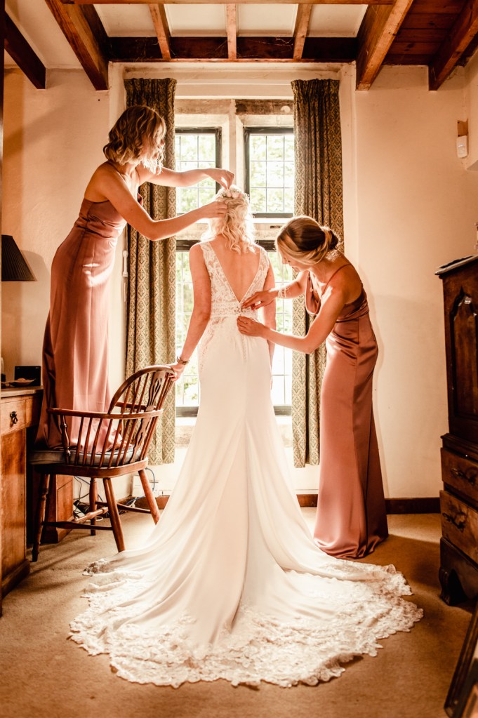 bride getting ready hepled by bridesmaids