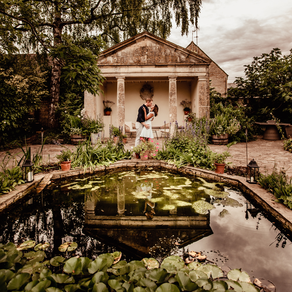 couple hugging front of temple and pond barnsley house hotel cotswolds