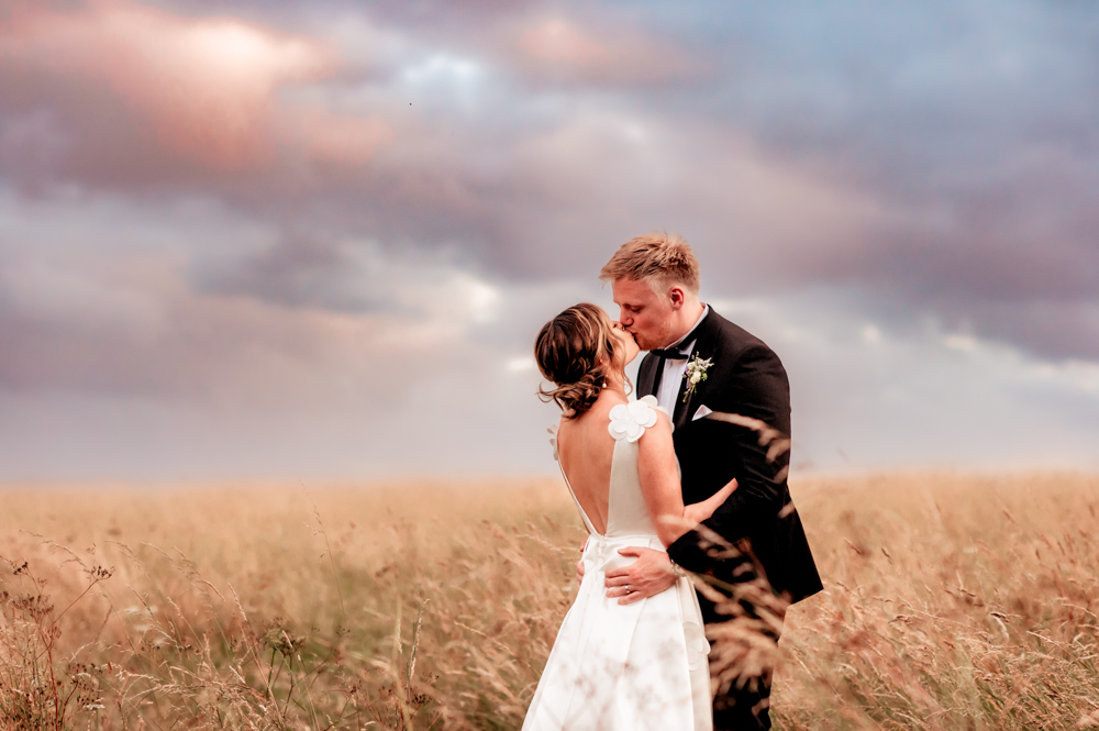 colourful sky meadow bride and groom kissing