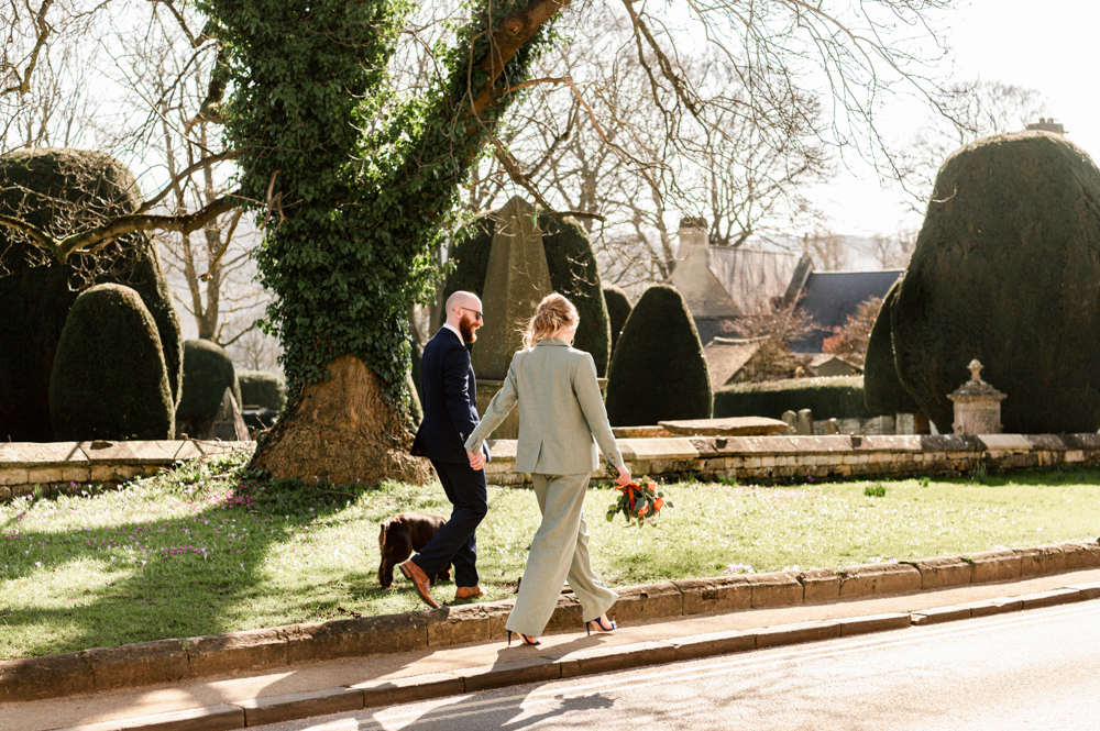 bride in green trouser suit walking in cotswolds village