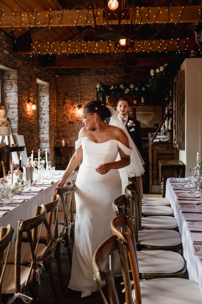 bride and groom walking between tables in a barn wedding venue south west england
