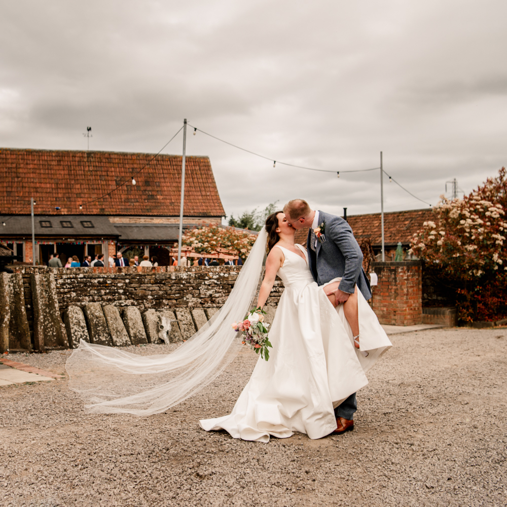 bride and groom kissing in from of  milton end barn wedding venue Gloucestershire uk