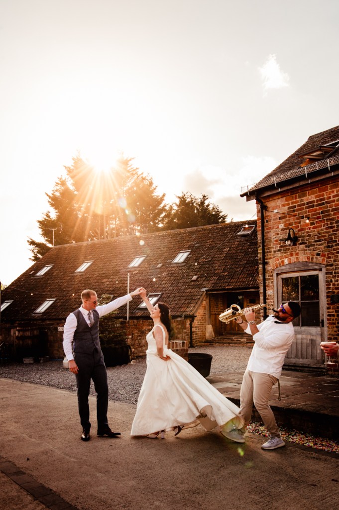 bride and groom dancing to saxophone outside at sunset moody wedding at milton end barn 