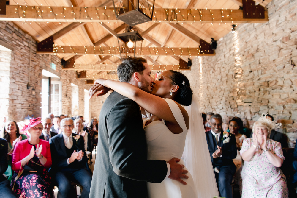first kiss of bride and groom in a rustic barn cotswolds