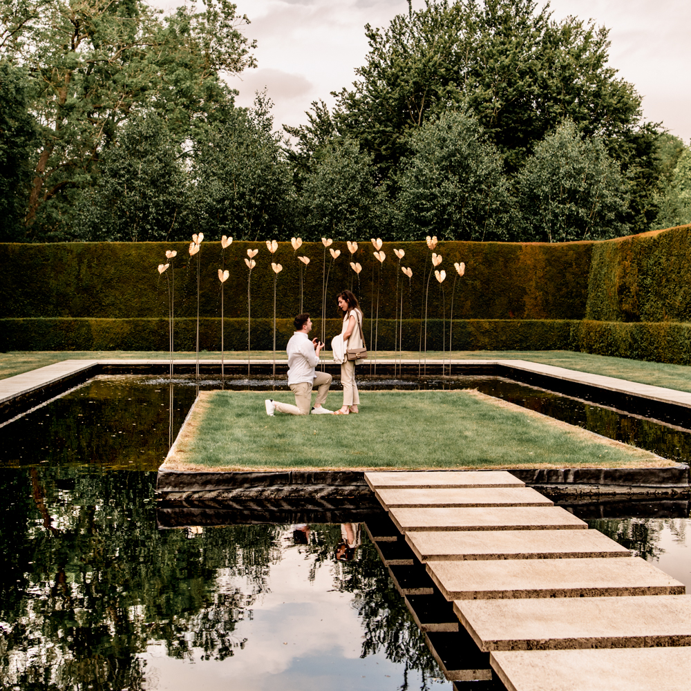 man down on one knee proposing in a garden with water feature