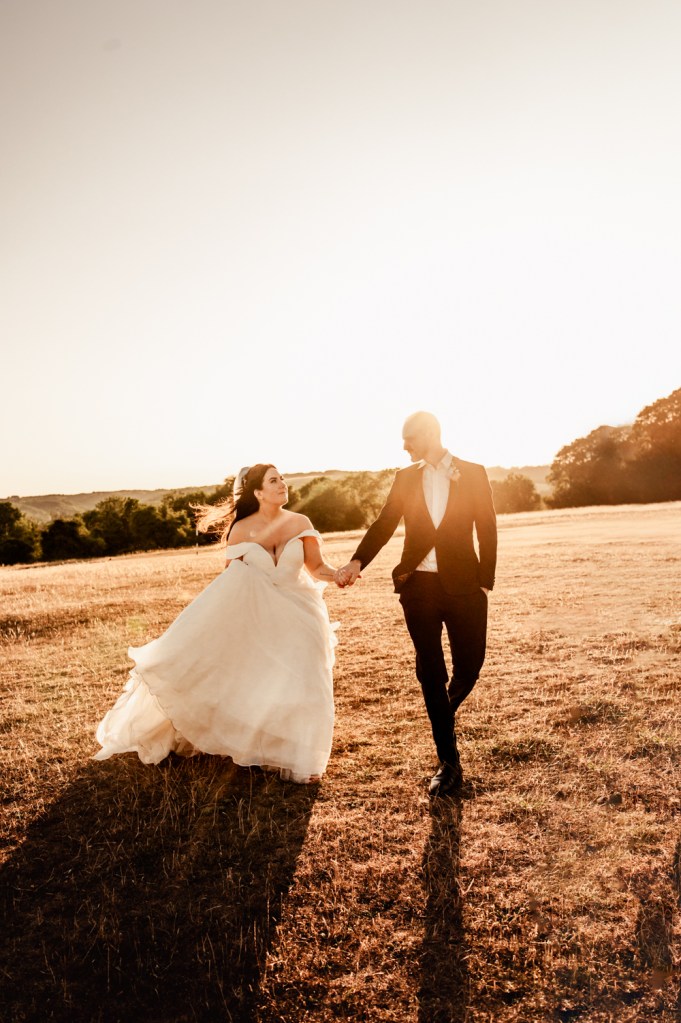 bride and groom walkiing in a field cotswolds
