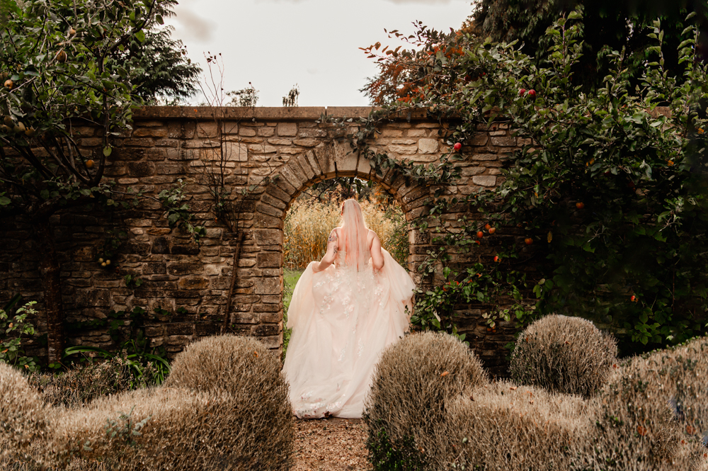 bride walking through an arch dreamy garden cotswolds
