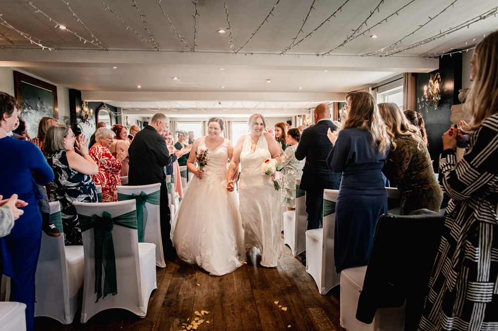 two brides in wedding dresses walking ceremony