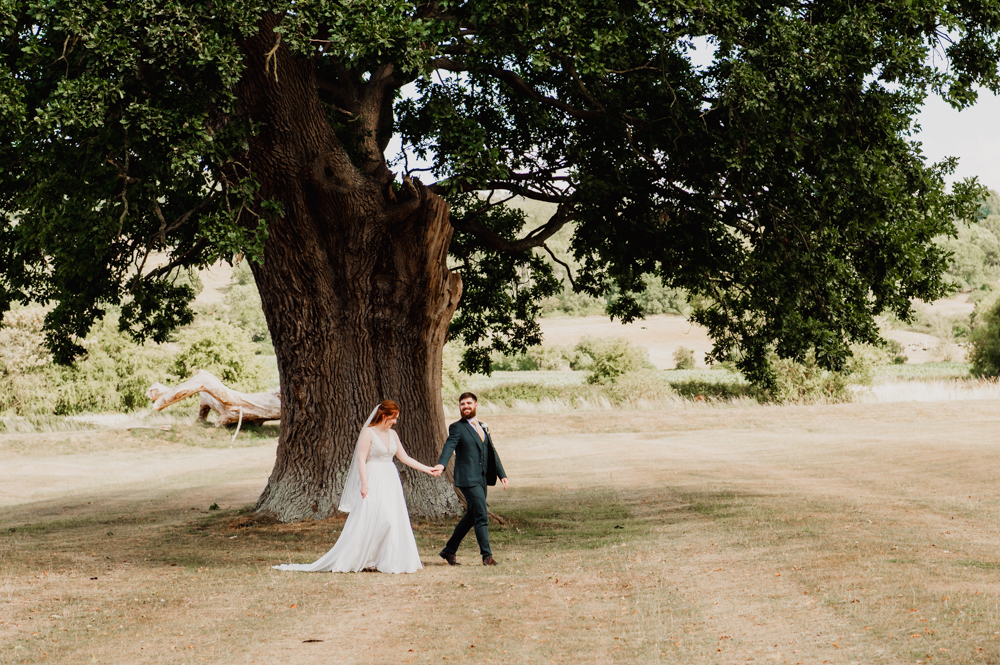 Bride and groom walking in the countryside under a big tree Cotswold wedding photographer