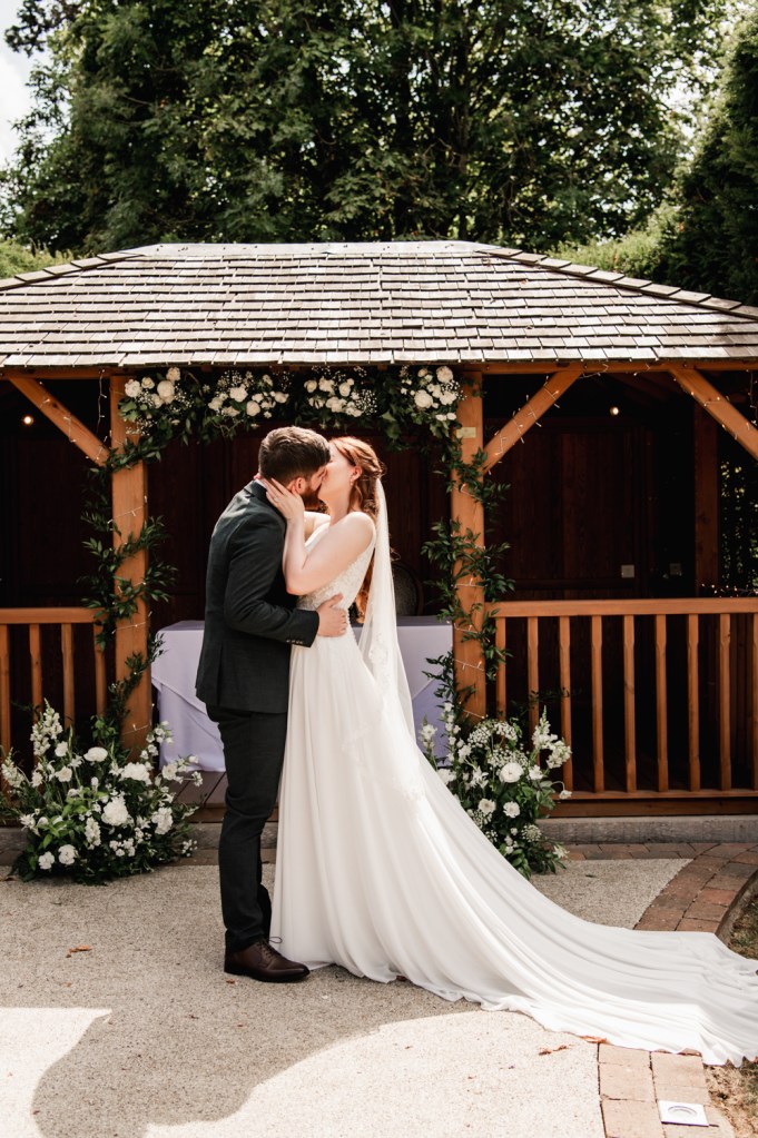 Bride and groom kissing during the outdoor ceremony at The Greenway Hotel captured by Cheltenham wedding photographer