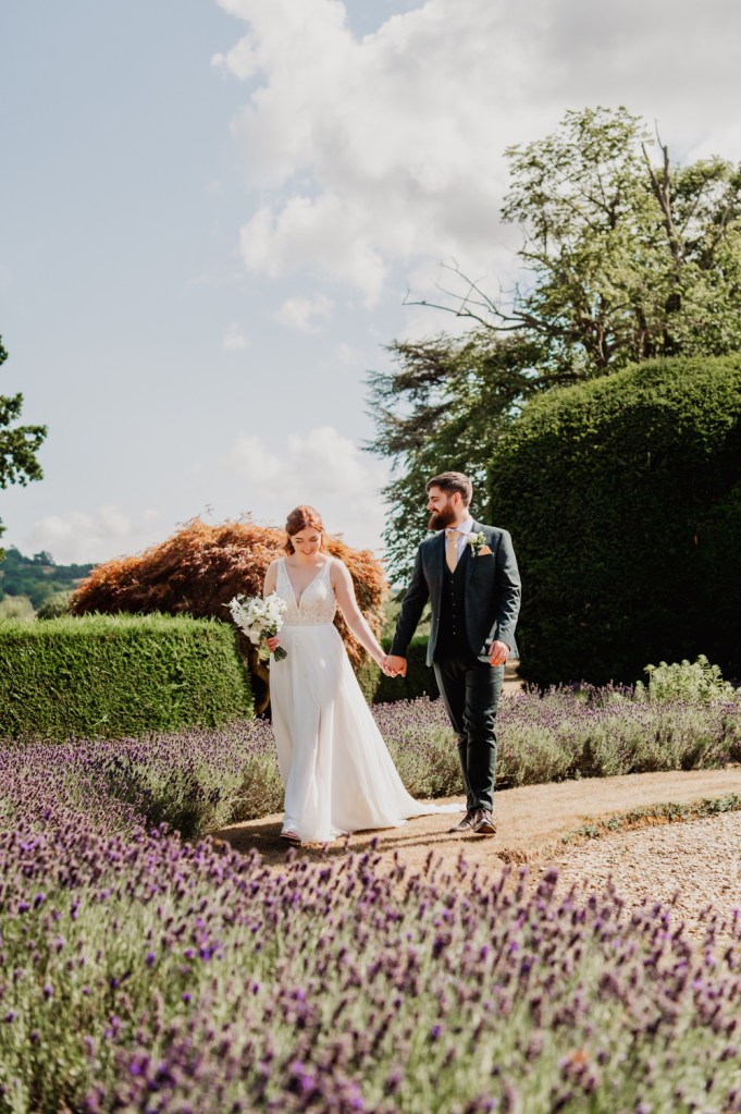 Bride and groom walking in a summer garden in the countryside captured by Cotswold wedding photographer