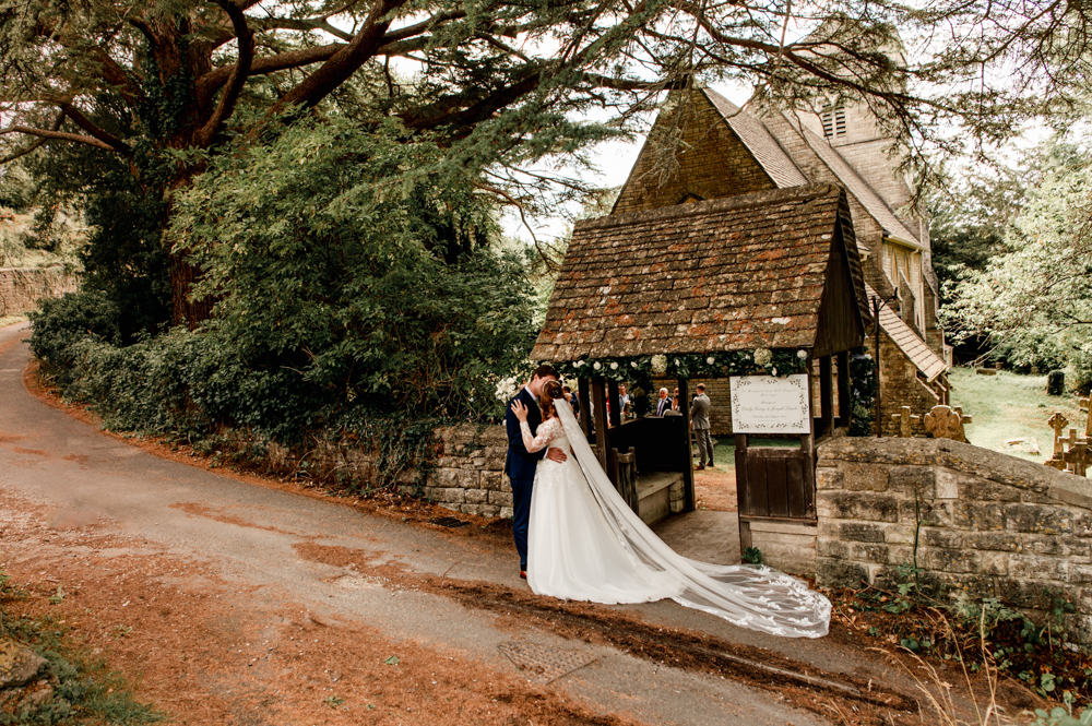 bride and groom kissing in front of a romantic church Cotswold
