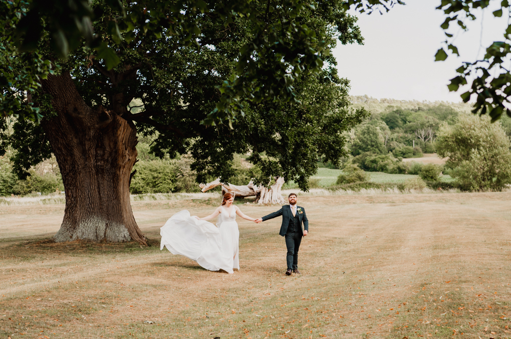 Bride and groom walking in the countryside captured by Cotswold wedding photographer