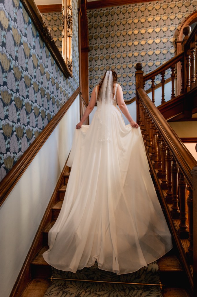 Bride walking up an elegant staircase of a manor house hotel  captured by Cotswold wedding photographer
