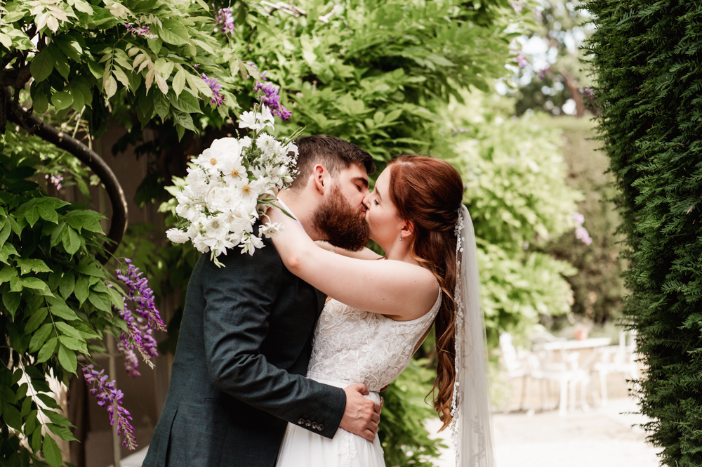 Bride and groom kissing under wisteria at The Greenway Hotel in the Cotswolds